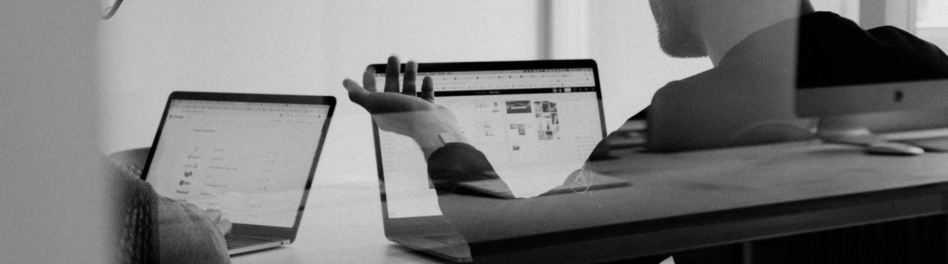 Duas pessoas a trabalhar em frente a computadores portáteis, a visualizar páginas e dados, num ambiente de escritório moderno.